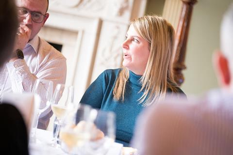 Photograph focused on RGI Solutions director Sarah Glenn, talking to an attendee to her right at the roundtable. She wears a teal turtle-neck jumper.